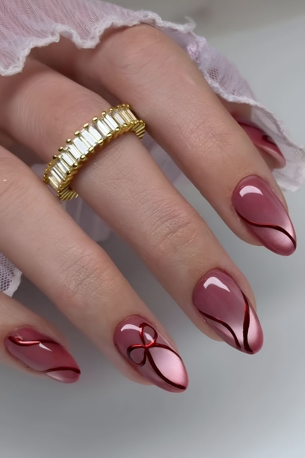 Light red nails with a metallic red bow and swirls