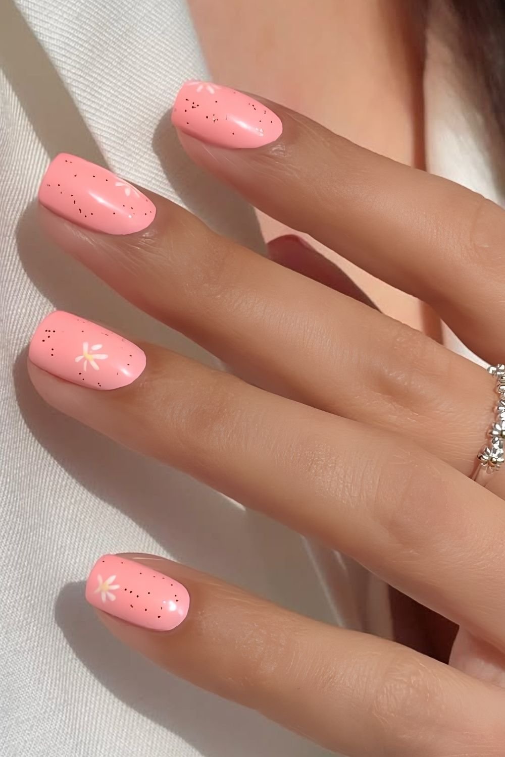Pastel peach nails with white daises and tiny black speckles