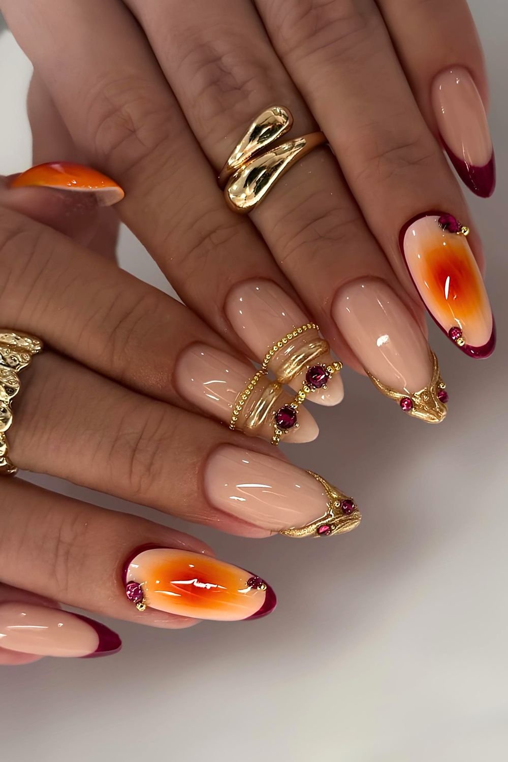 Orange aura nails with dark red and gold french tips and golden nail ring accents