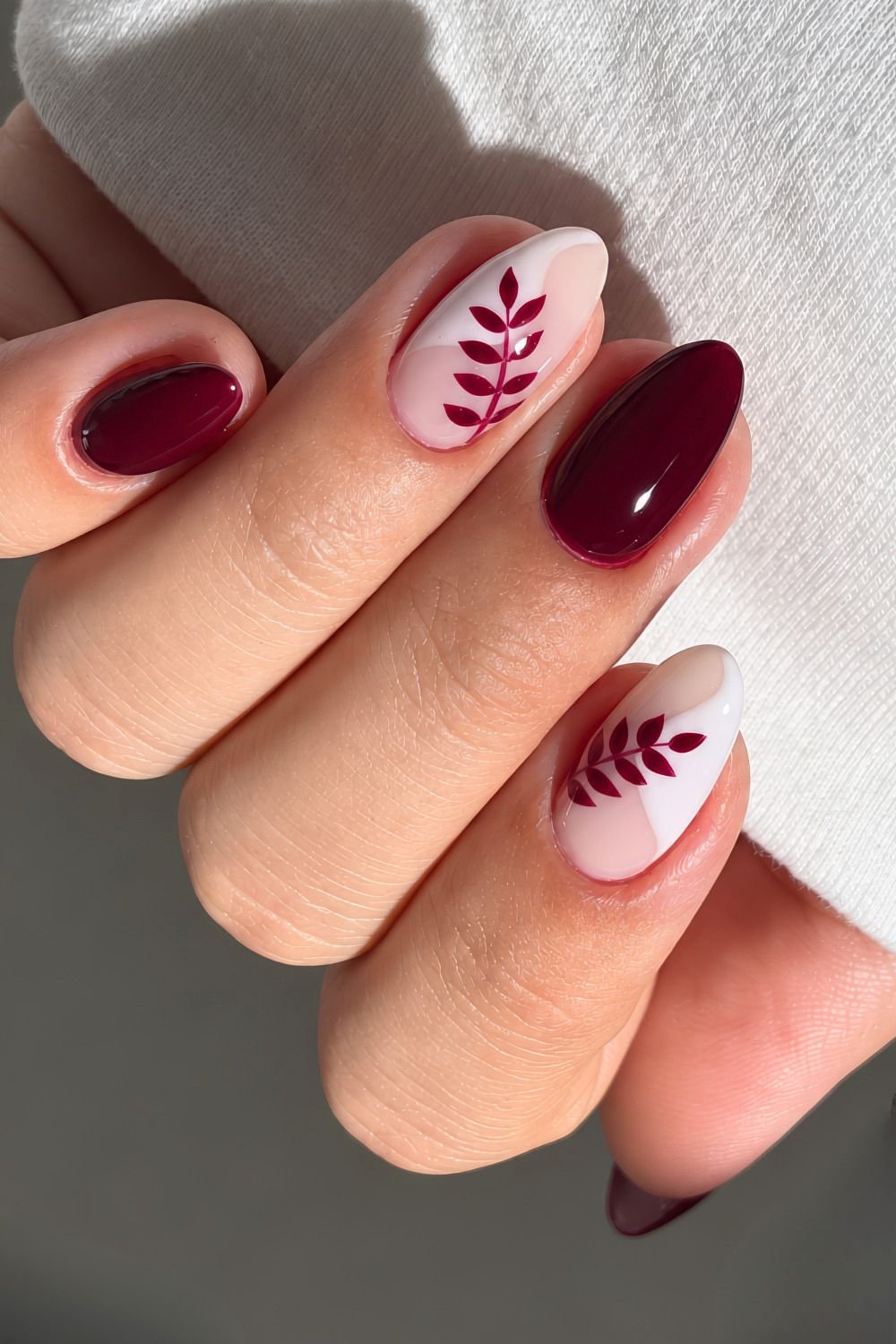Deep cherry red nails with leaf accents on a white abstract base